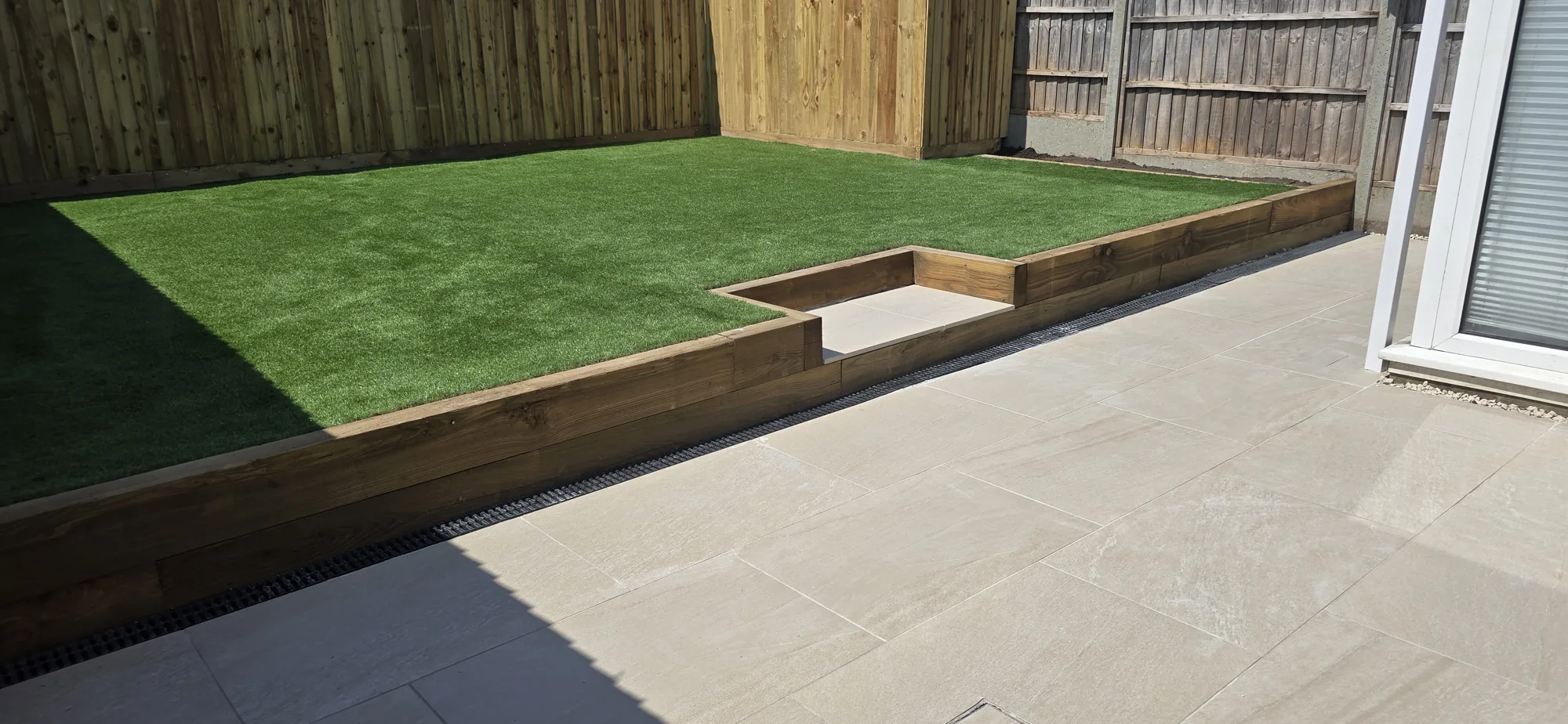 Sandstone patio with sleeper-edged lawn in a landscaped Surrey garden by Siviter Projects