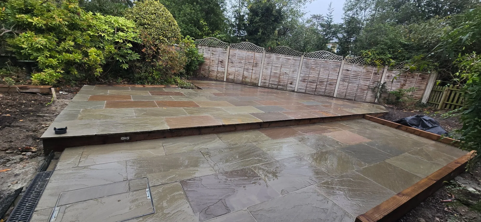 Finished two-level Raj blend sandstone patio with softwood sleeper edging in a Camberley garden