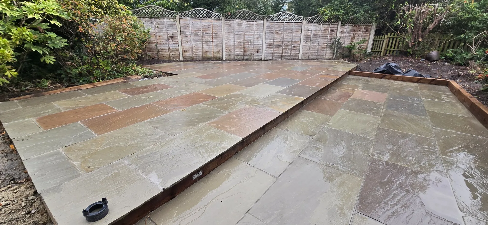 Sandstone step and softwood sleeper edge between the two patio levels in Surrey