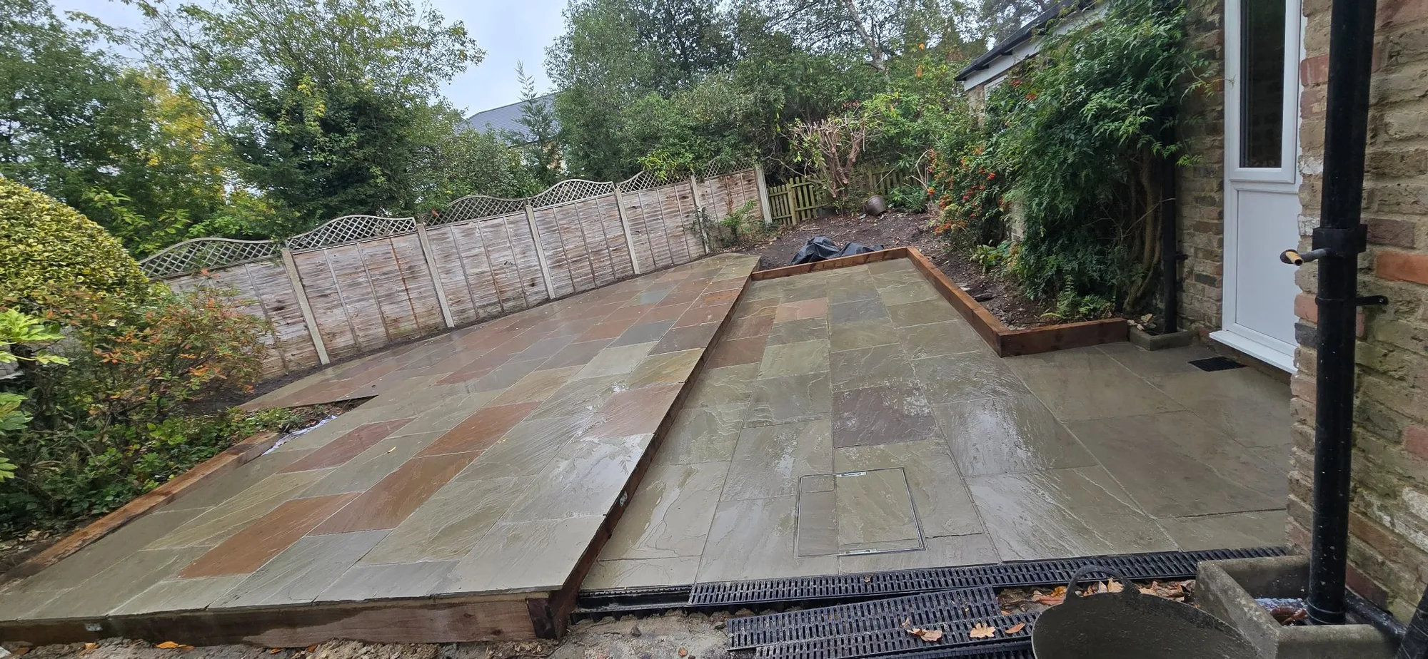 Two-level Raj blend sandstone patio with softwood sleeper beds in a landscaped Camberley garden by Siviter Projects