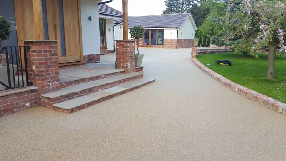 Buff resin-bound driveway with brick edging and sandstone steps leading to a house in Surrey