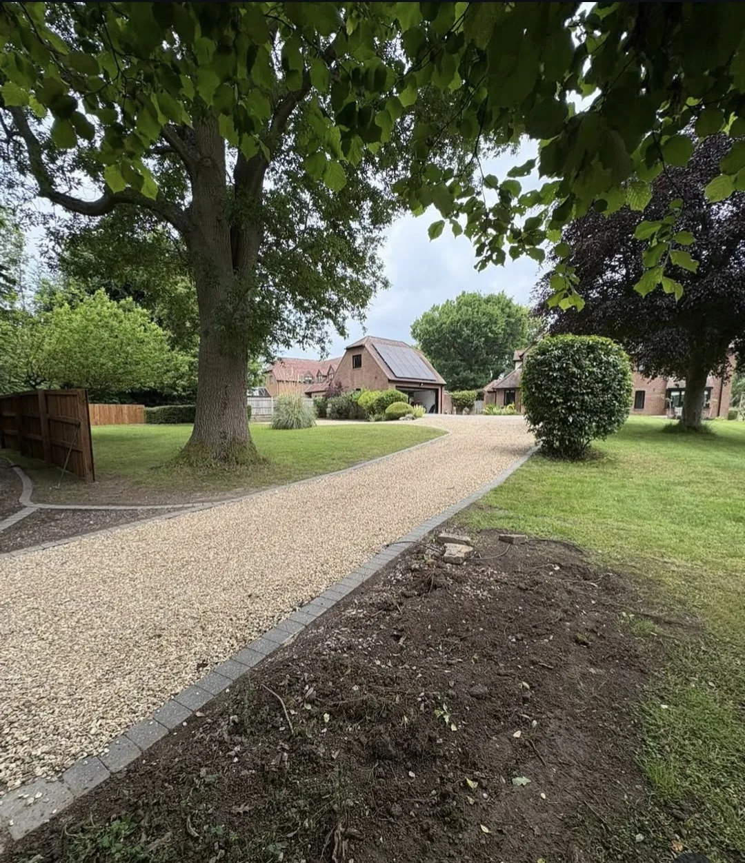 Long gravel driveway with block-paved edging winding through a tree-lined Surrey garden