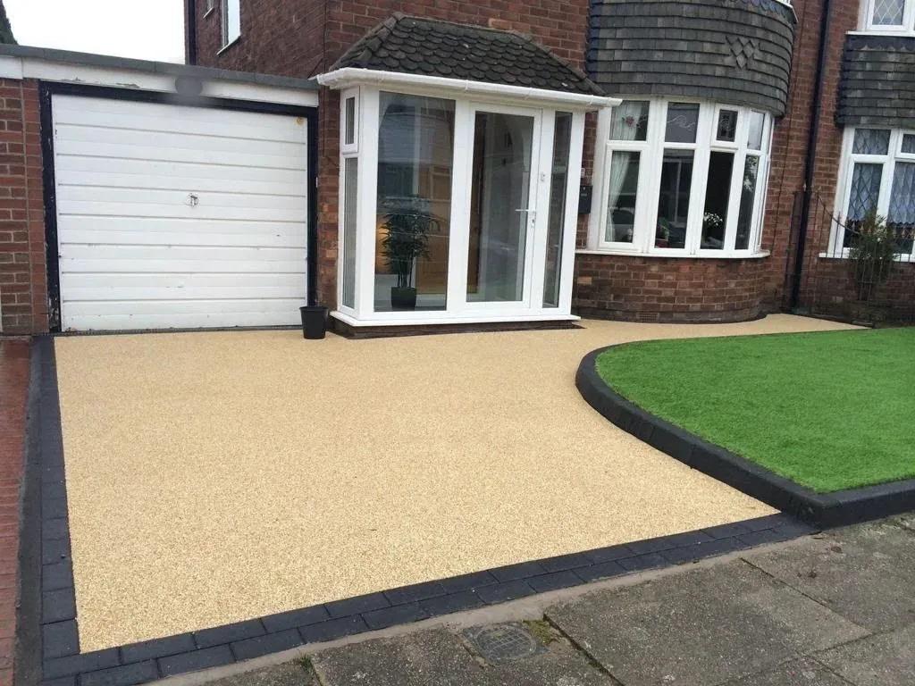 Buff resin driveway with block-paved edging beside a white garage door in Surrey