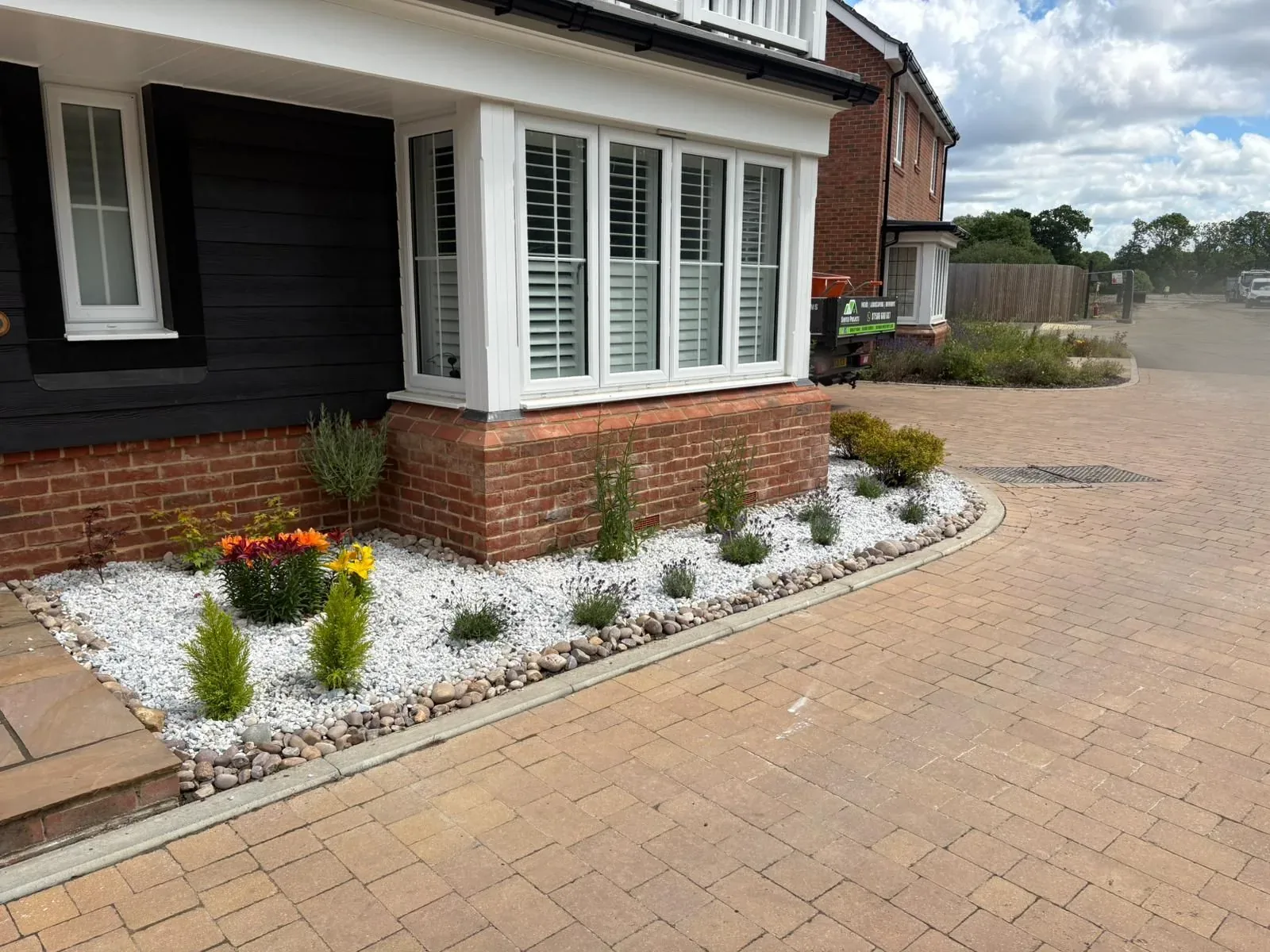 Block-paved driveway with a planted border and decorative stone beside a bay window