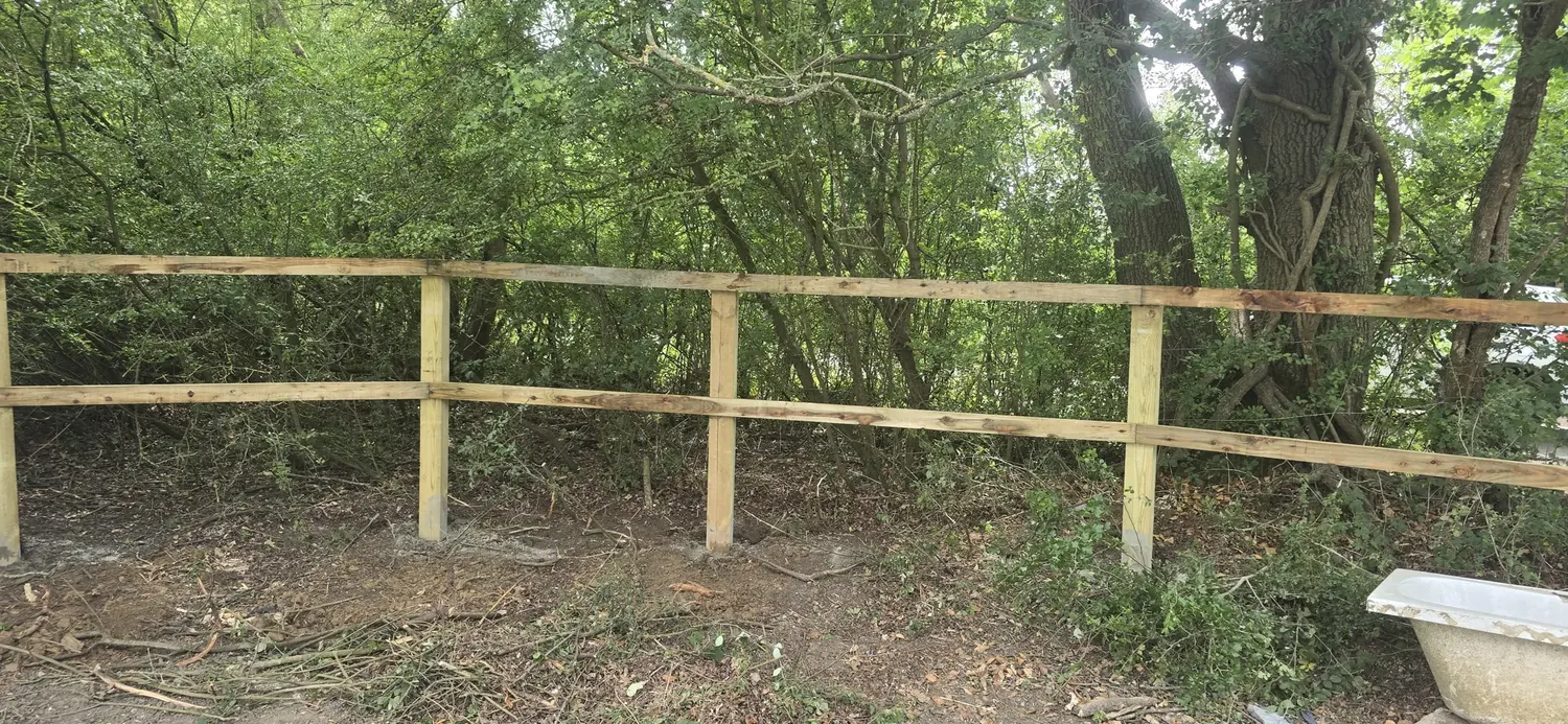 Newly installed post and rail timber fence along a rural woodland boundary