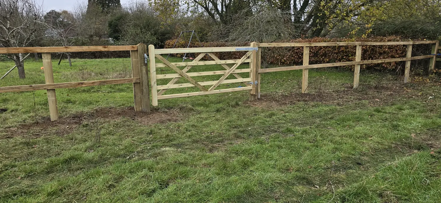 Post and rail paddock fencing with a wooden field gate in a Surrey meadow