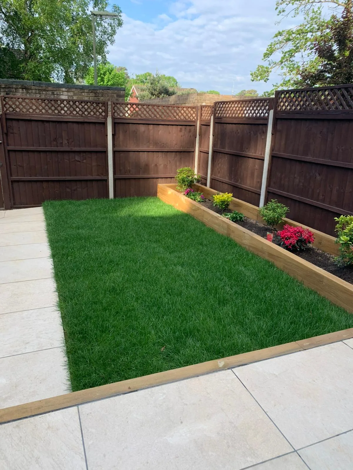 Dark stained close-board fence panels with lattice tops beside a new lawn and paved patio