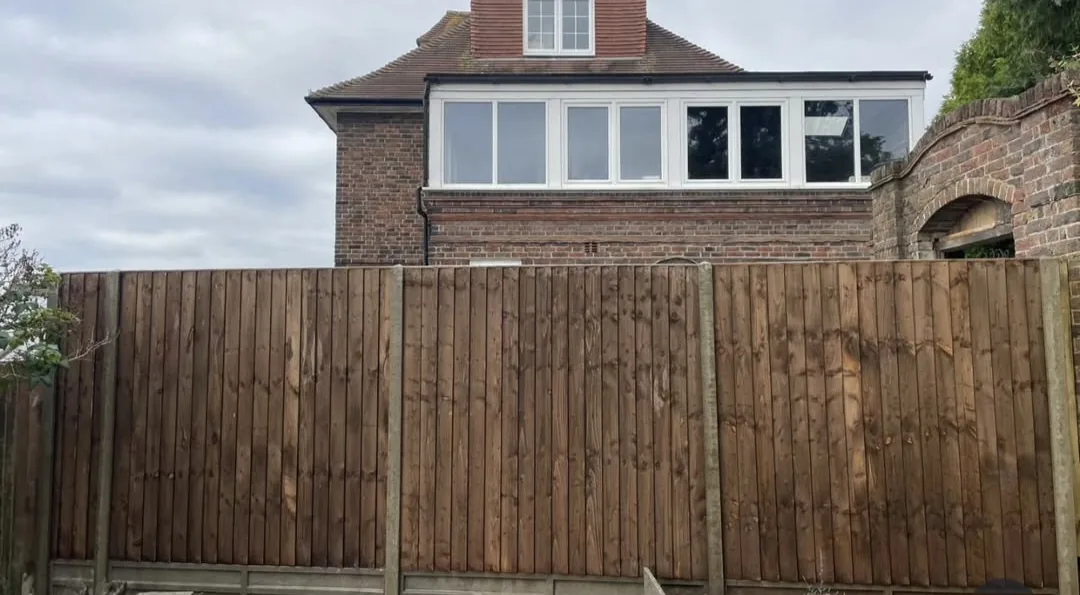 Dark brown close-board timber fence run in front of a brick house