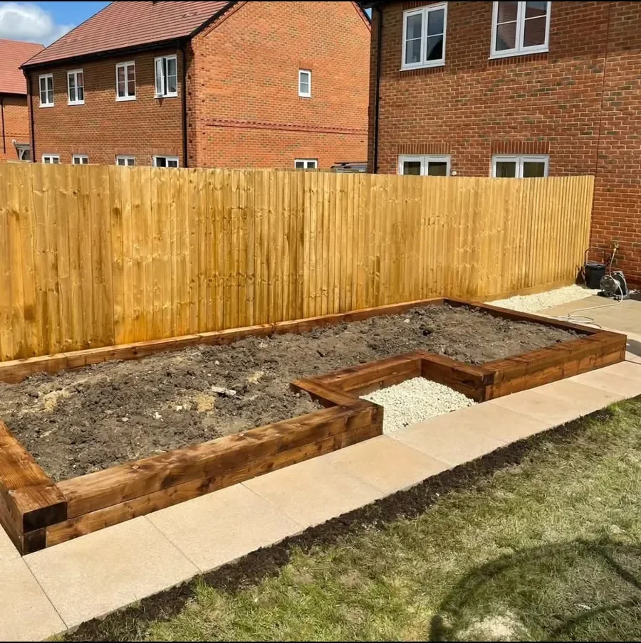 Close-board fence beside a new sleeper raised bed and paving in a rear garden