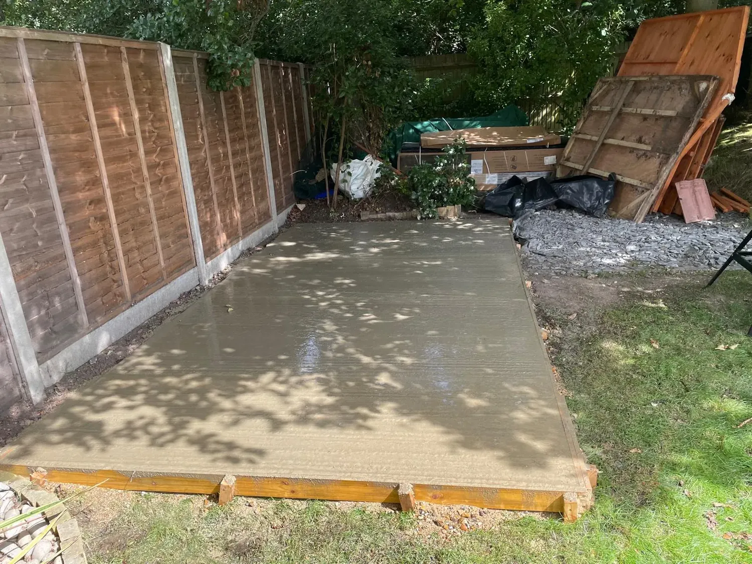 Completed concrete shed base cast in timber formwork in a fenced Surrey garden