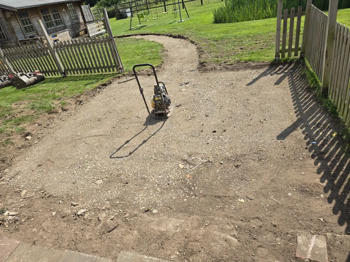 Wacker plate compacting a curved sub base pathway across a garden during groundworks