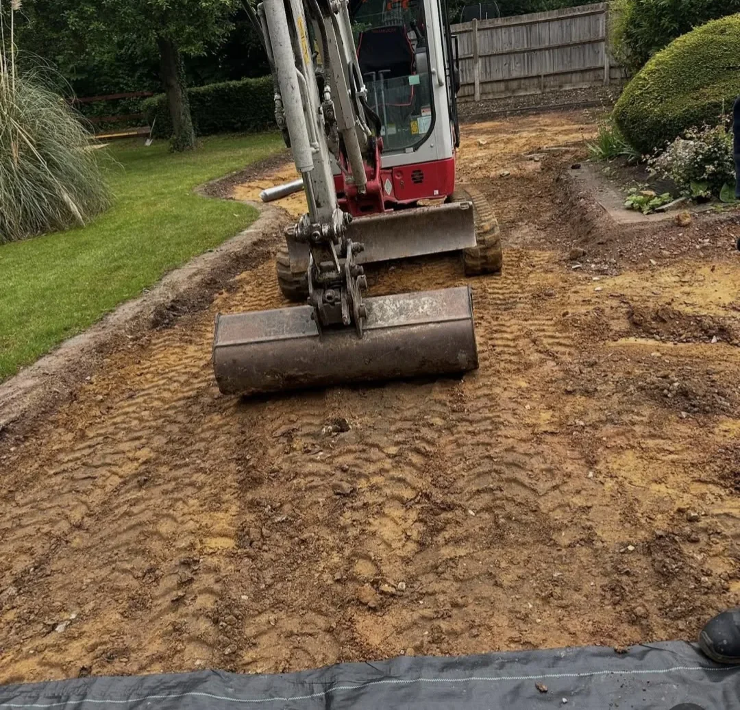 Mini excavator levelling excavated ground in a garden during groundworks