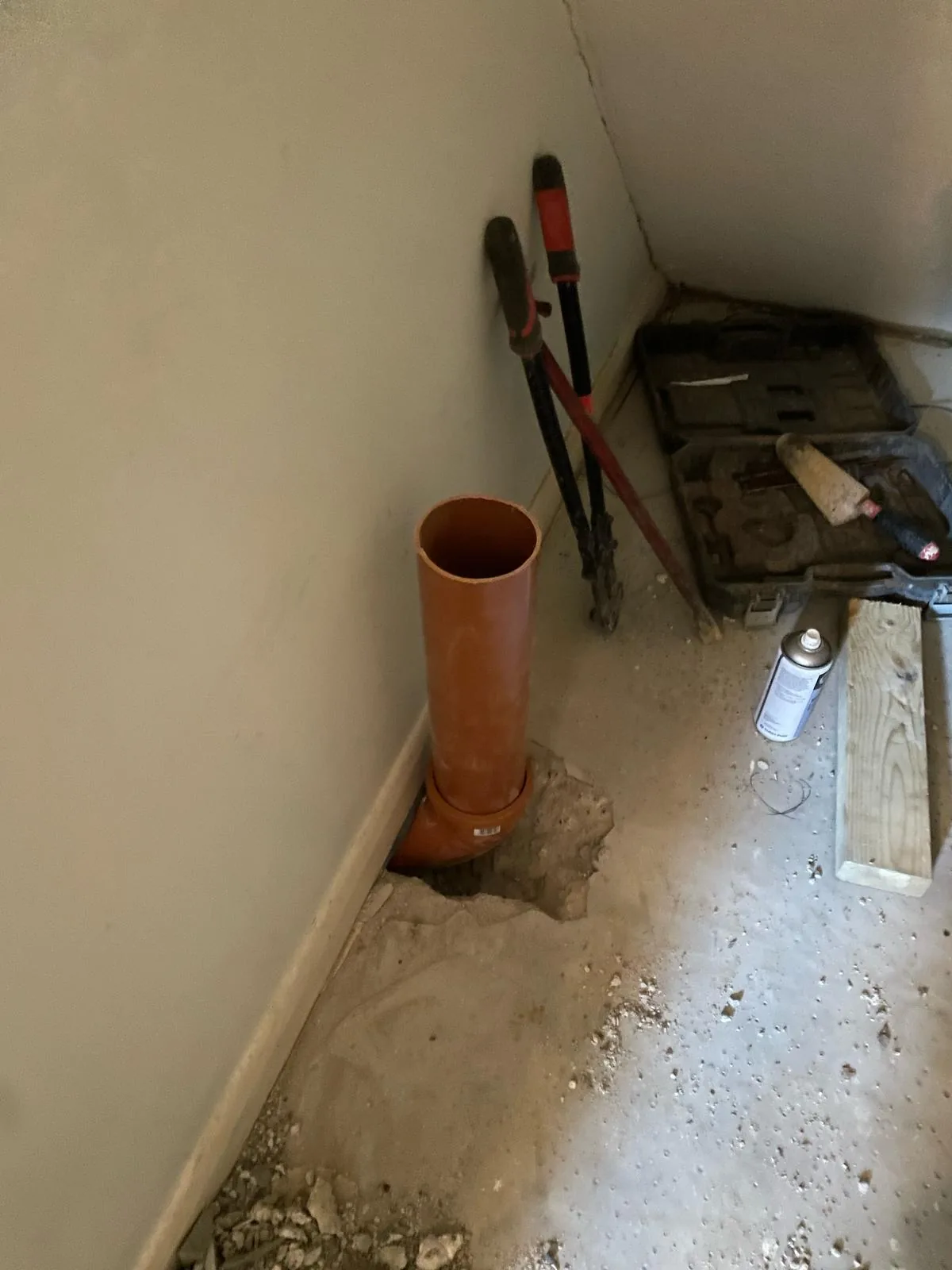 Orange soil pipe installed through a broken out concrete floor during internal drainage works