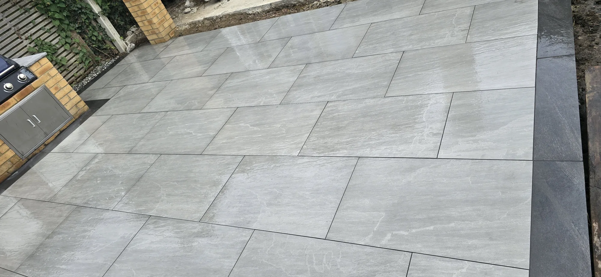 Grey riven porcelain patio with charcoal border and brick outdoor kitchen in a Surrey garden