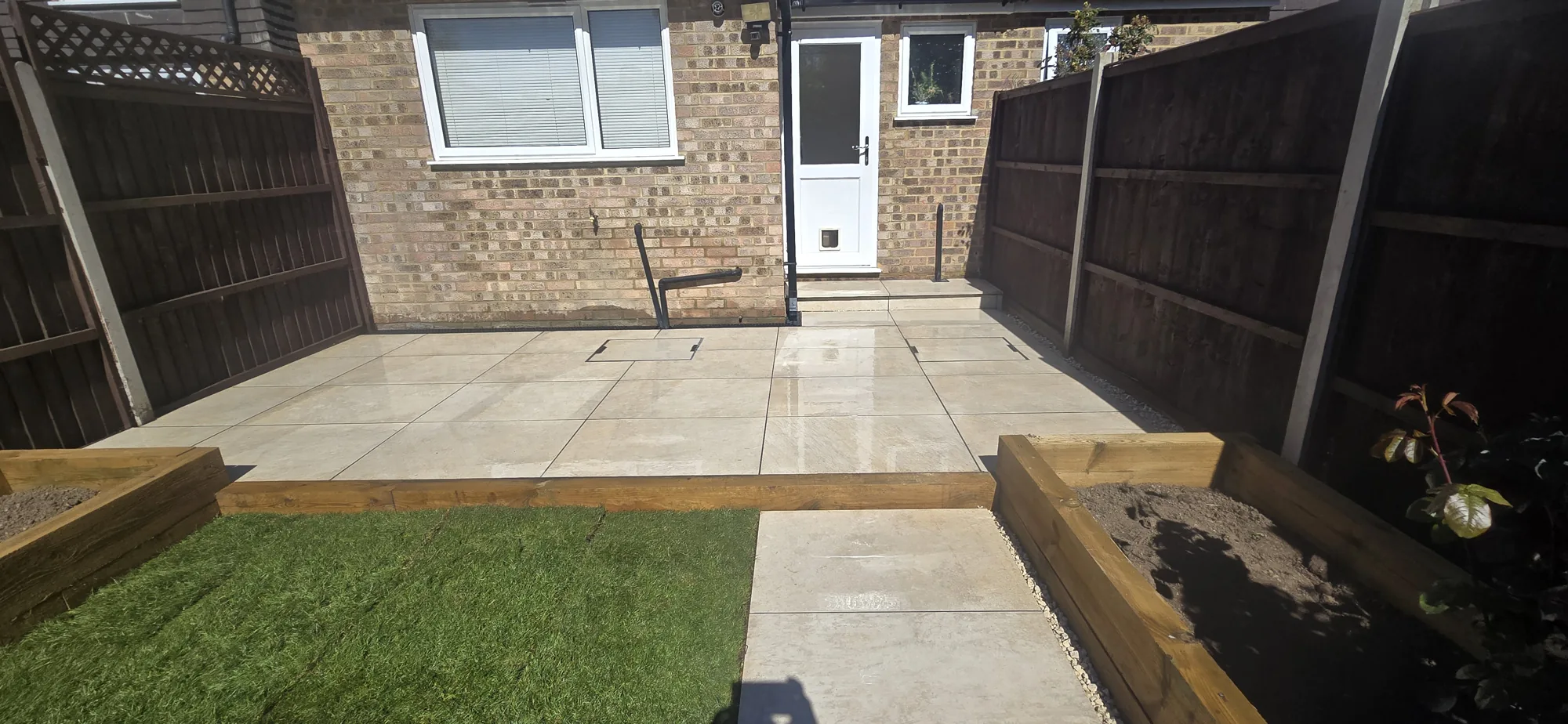 Cream porcelain patio with timber sleeper raised beds behind a brick home in Surrey