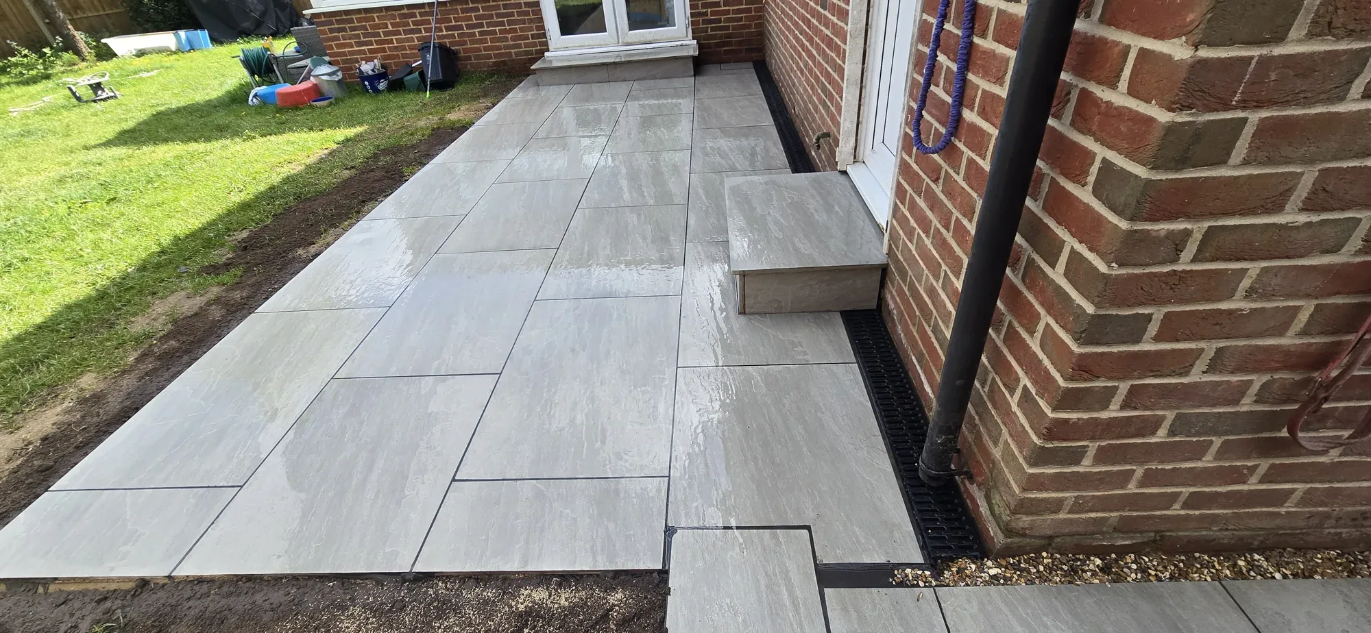Grey sandstone patio path with channel drainage alongside a red brick house in Surrey