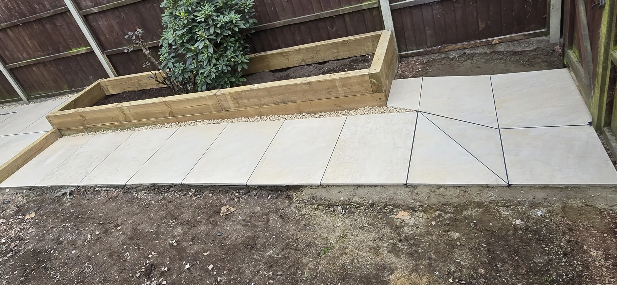 Cream sandstone paving beside a timber sleeper raised bed in a Surrey garden