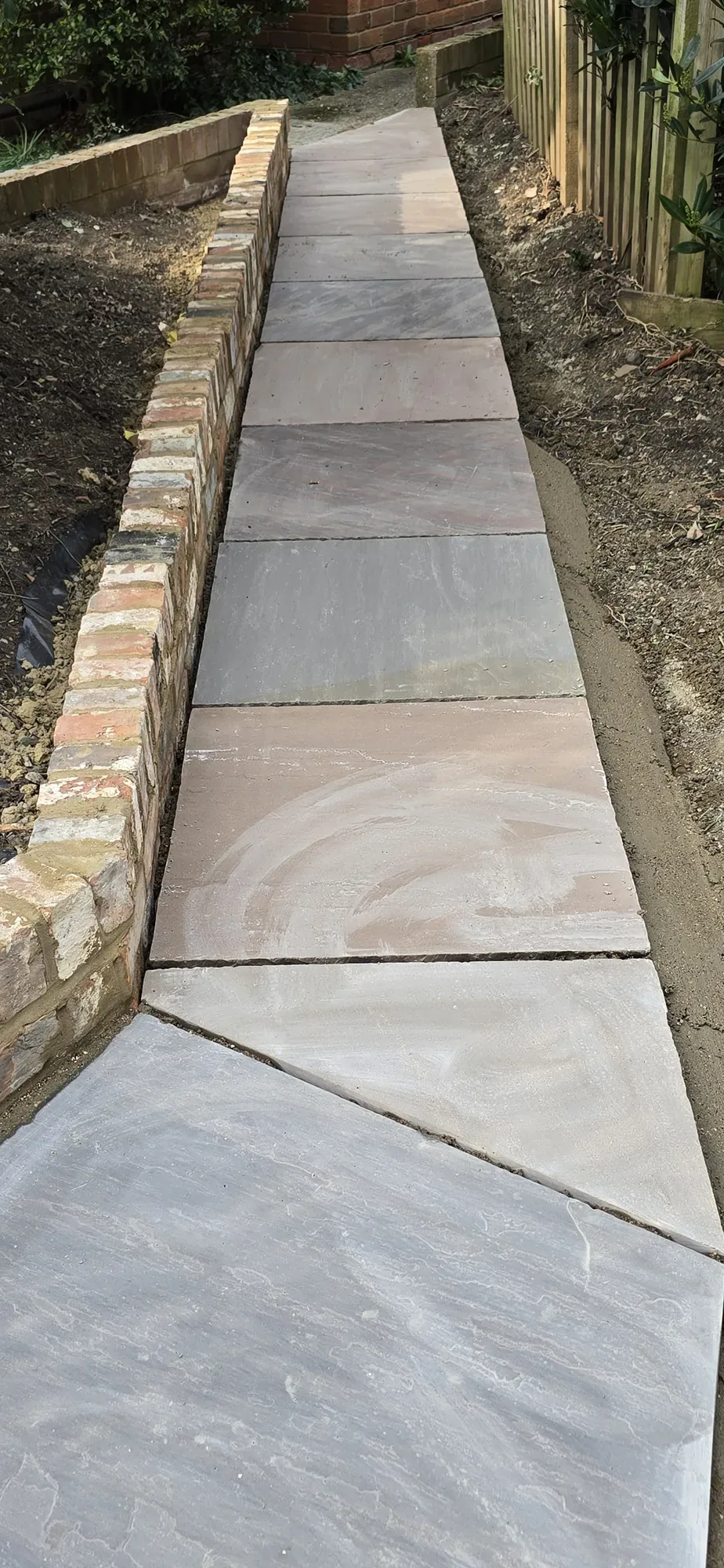 Multi-tone Indian sandstone slabs laid against brick edging during a Surrey patio installation