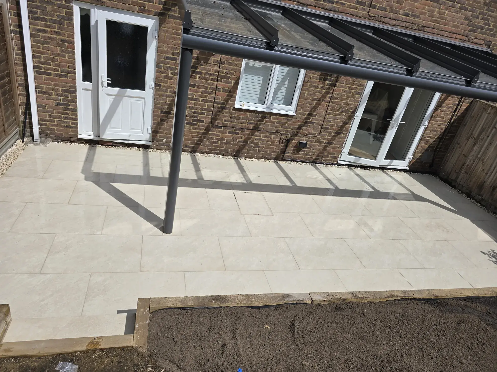 Cream travertine-effect porcelain patio under a glass veranda against a brick house in Surrey