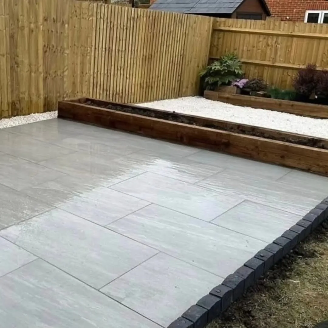 Grey porcelain patio with charcoal sett edging and sleeper raised beds in a Surrey garden